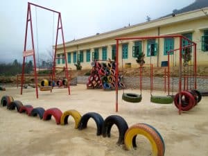 Lăn bánh ước mơ %Sân chơi %Tái chế%Trẻ em %Niềm vui Toàn cảnh sân chơi lốp xe tái chế với xích đu, cầu treo và các hạng mục vận động tại điểm trường vùng cao